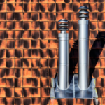 Two metal pipes forming a part of a plumbing system on top of a tiled roof.