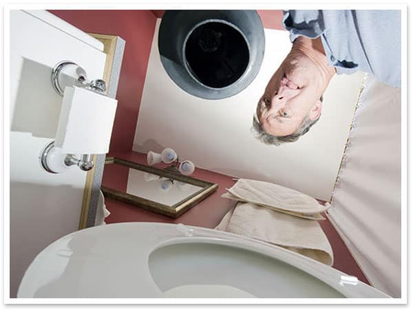 A man is standing by the malfunctioning toilet in a bathroom.