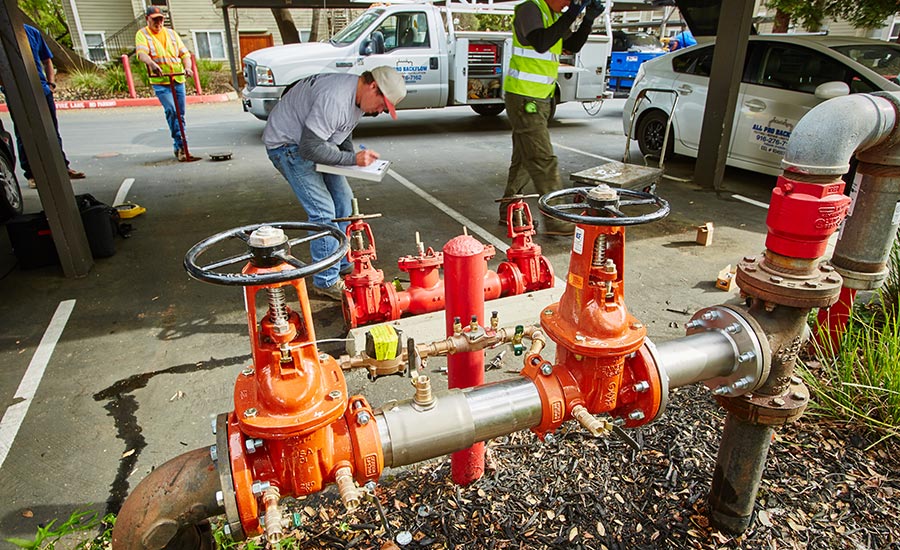 A man is working on a sprinkler piping system in front of a car.