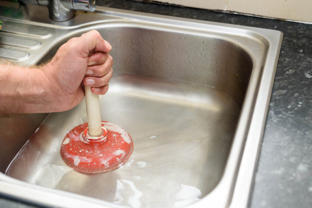 A person cleaning a clogged drain with a plunger.