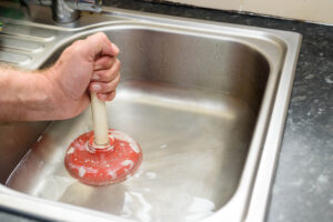 A person cleaning a clogged drain with a plunger.