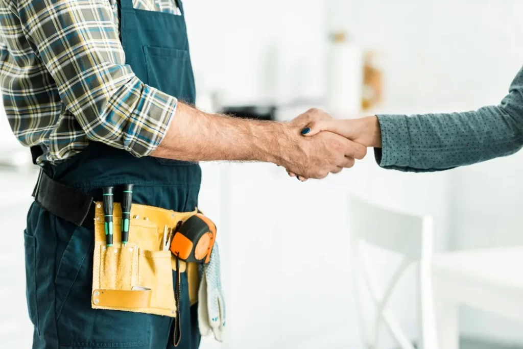 A plumber and woman shaking hands in front of a kitchen.