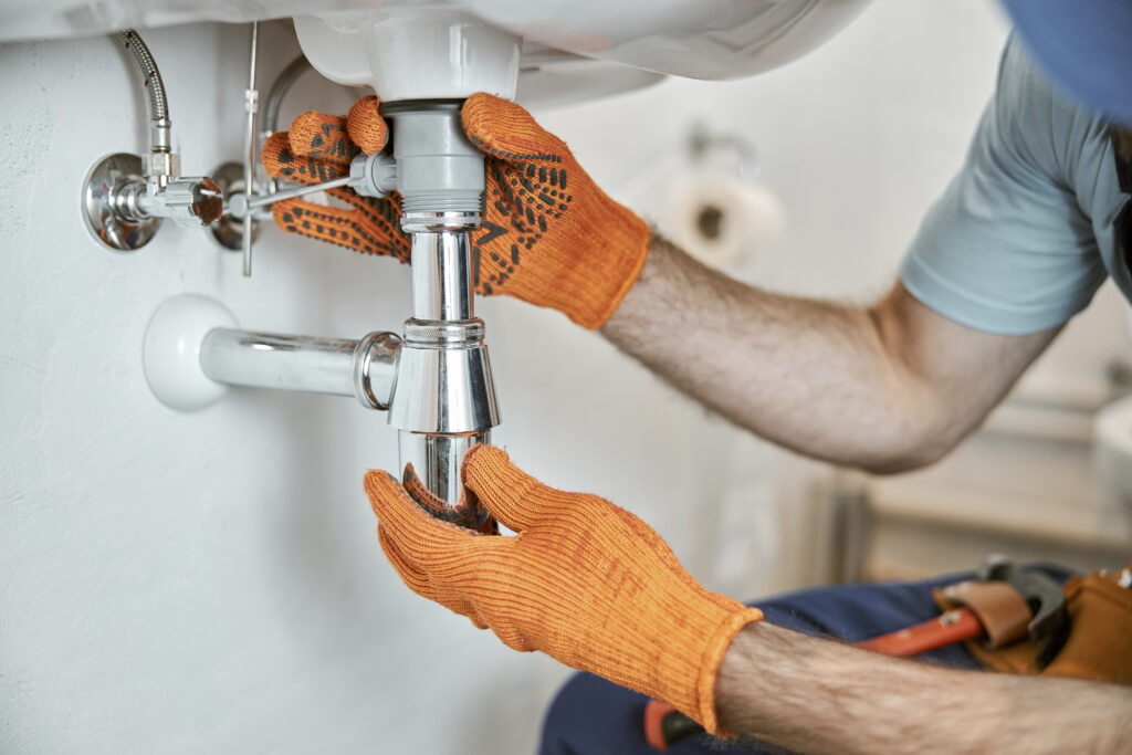 A plumber providing residential plumbing services fixing a sink in a bathroom.