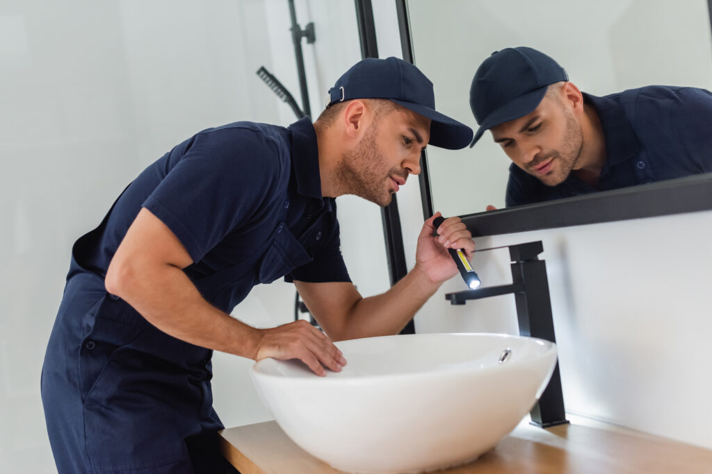 plumber checking sink with flashlight in modern bathroom