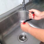 A person is using a tool for drain cleaning to clean a sink.