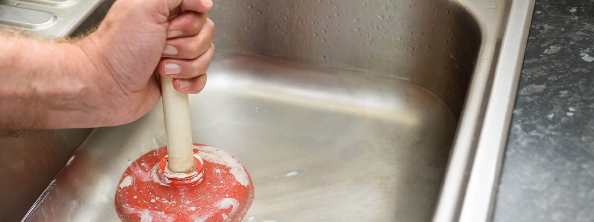 A person cleaning a clogged drain with a plunger.